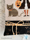 Close-up of the Moonlight Mischief Halloween cross stitch pillow showing the gray cat, striped baker's twine bow, and black coordinating fabric used to finish the pillow.