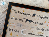 Close-up of 'Tis the Night Halloween cross stitch showing a witch hat, black cat, broom, and smiling crescent moon.
